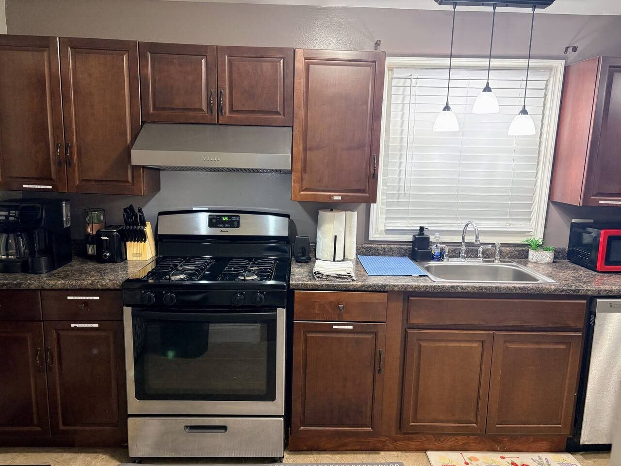 A kitchen with wooden cabinets, a stainless steel stove, a sink, and pendant lights.