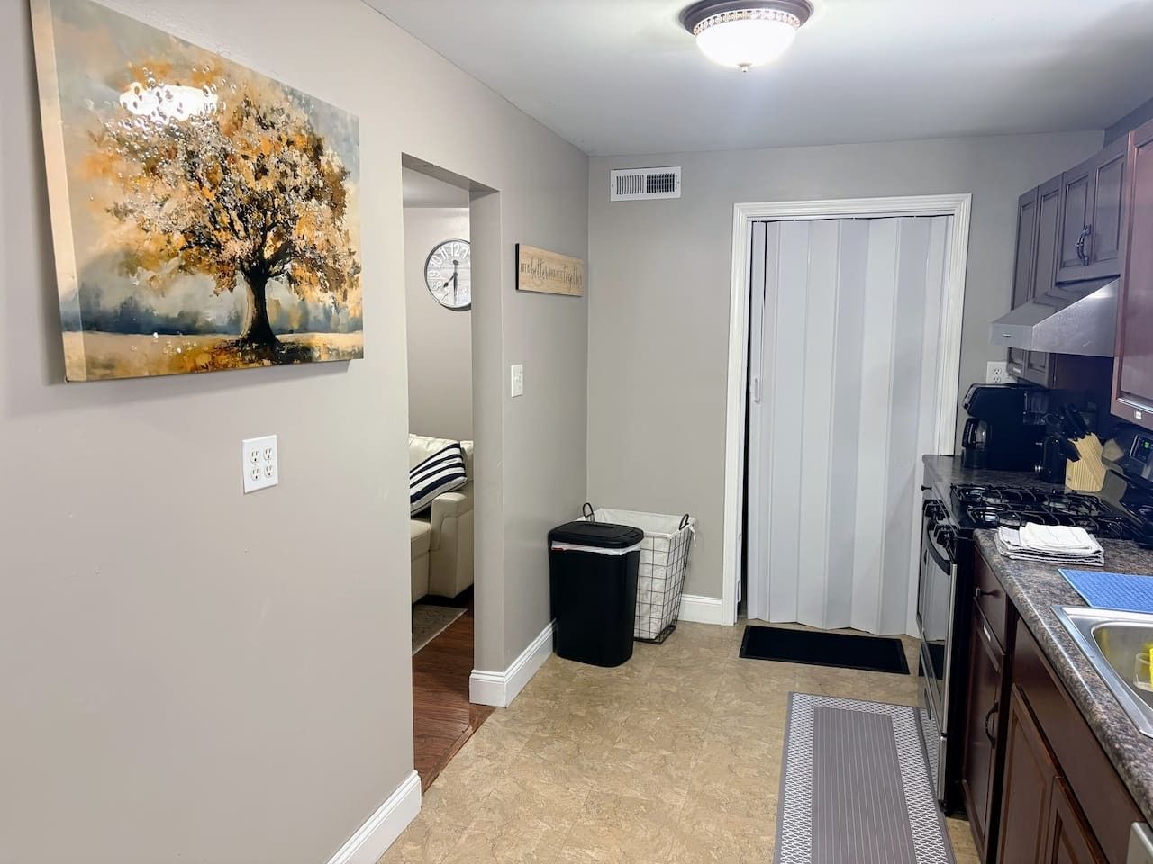 A kitchen with a stove, cabinets, and a countertop. There is a trash can and a laundry basket in the corner.