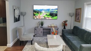 Un salon doté d’un téléviseur à écran plat, d’un canapé gris, d’un fauteuil et d’une table basse ornée d’un vase de fleurs.