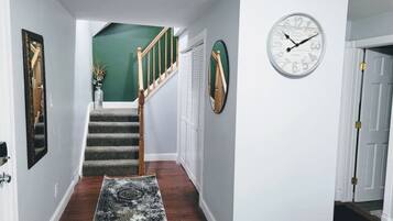 A hallway with a carpet, a staircase, a clock, and a door.