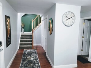 Un pasillo con alfombra, una escalera, un reloj y una puerta.