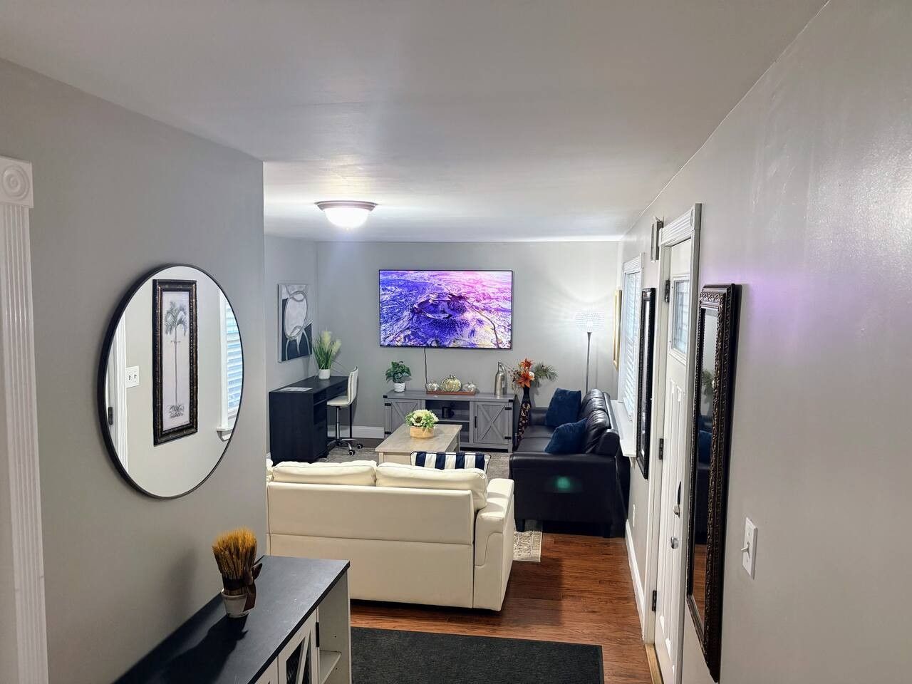 A modern living room with a sofa, a coffee table, and a TV. There is a mirror on the wall and a door leading to another room.