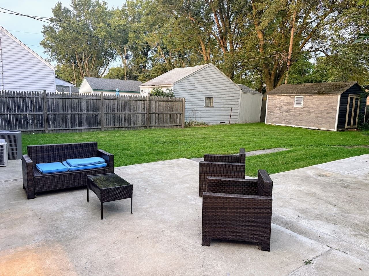 An outdoor patio area with wicker furniture, a concrete floor, and a wooden fence.