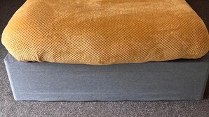 Un llit amb un panell frontal gris, una manta groga mostassa i dos coixins amb dibuixos de punts.