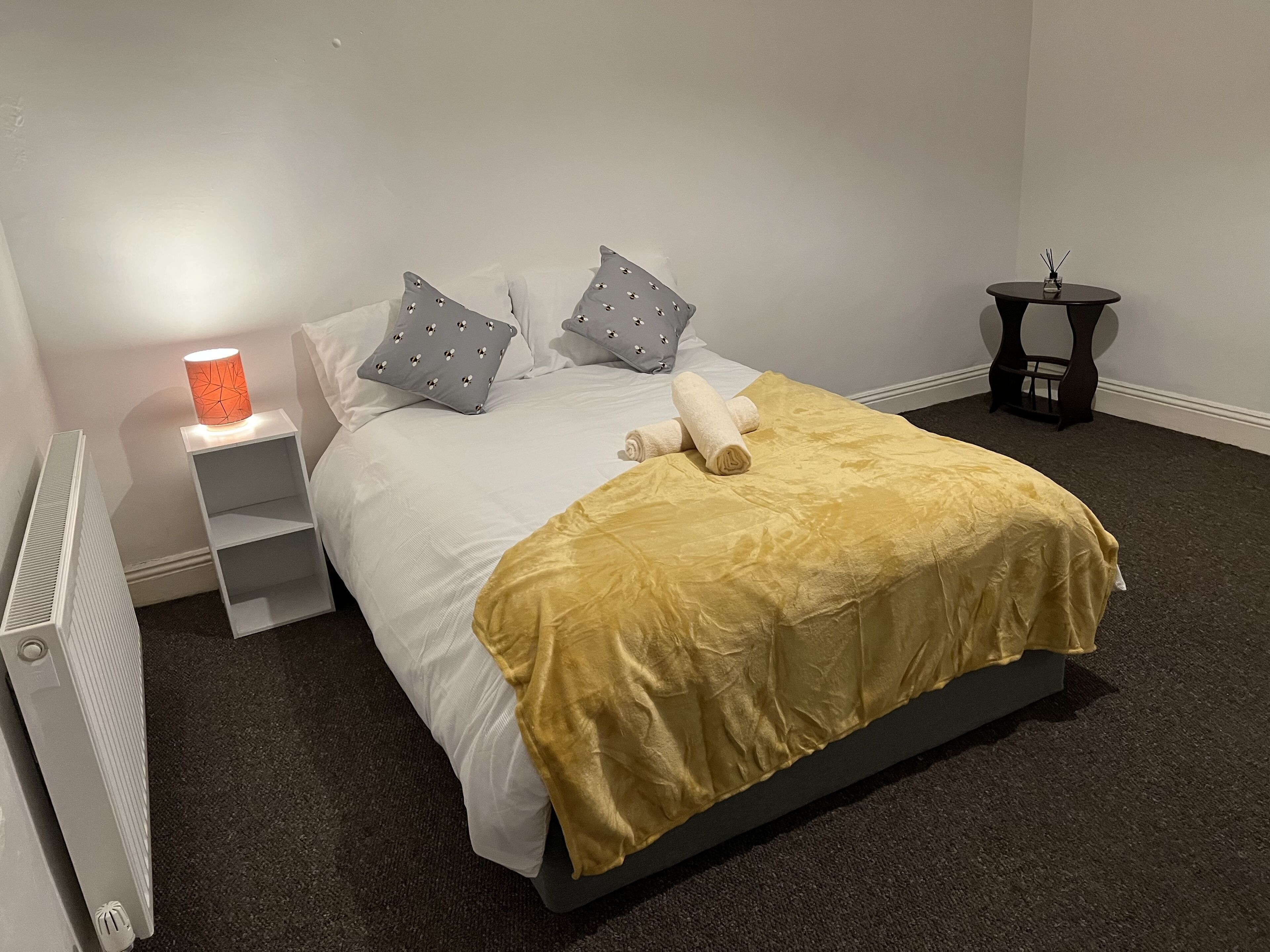 A neatly made bed with a yellow blanket, two pillows, and a bedside lamp.