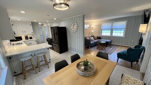 Una cocina moderna con una isla central, un comedor con mesa de madera y una sala de estar con sofá y un sillón estampado.