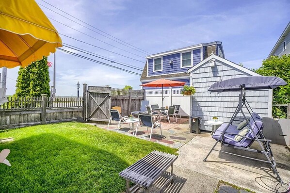 A backyard with a swing chair, a patio table, and a covered seating area.