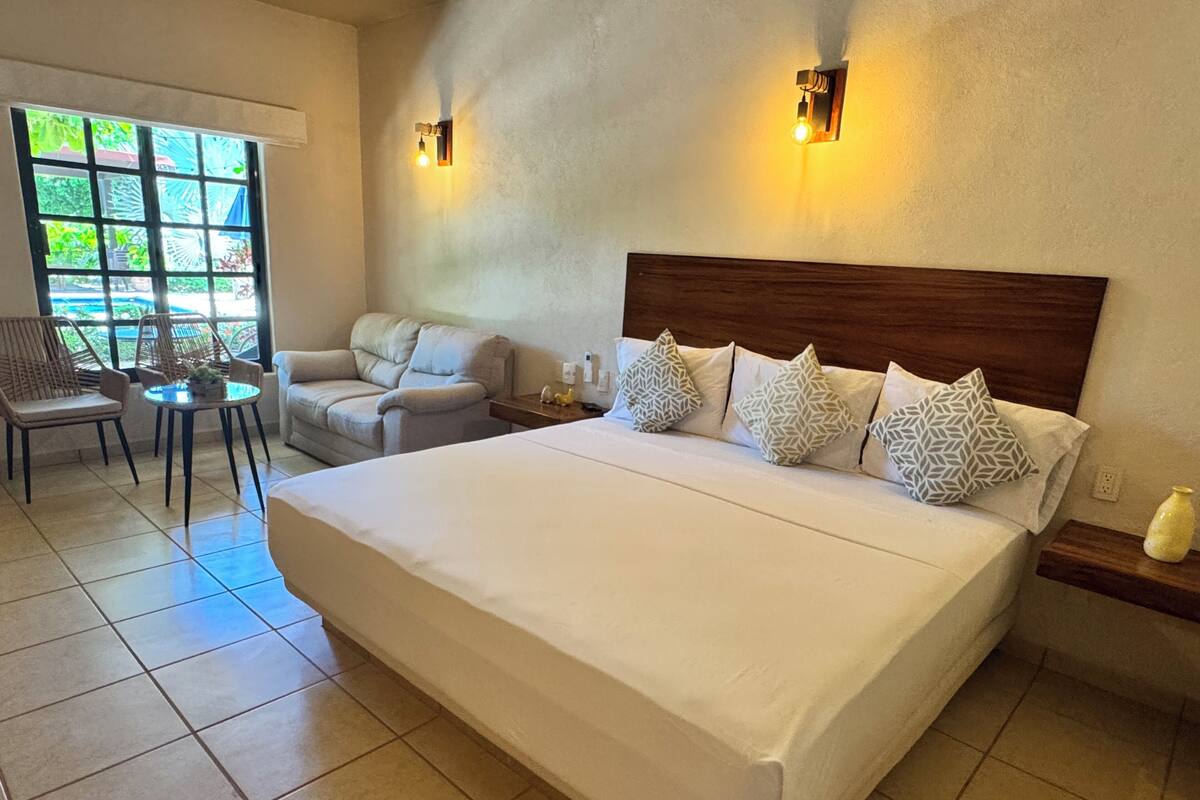 A hotel room with a large bed, a sofa, a small table, and two wall-mounted lights.