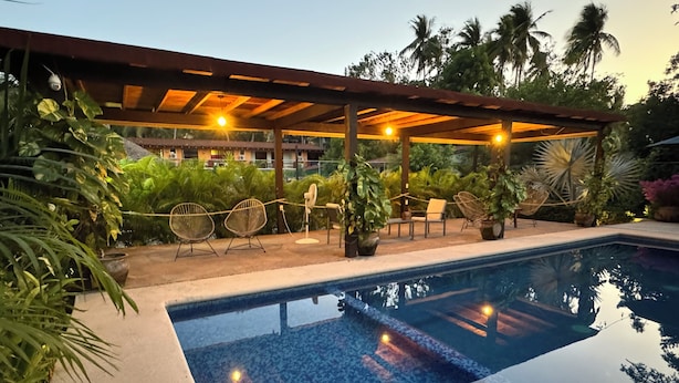 A pool area with a pergola, lounge chairs, and potted plants. - Natura Hotel y Villas  (Zihuatanejo)