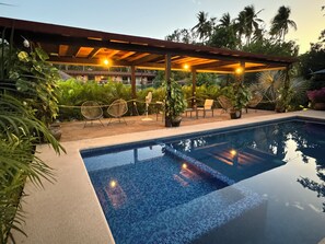 A pool area with a pergola, lounge chairs, and potted plants. - Natura Hotel y Villas  (Zihuatanejo)