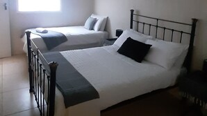 A bedroom with two single beds, a window with blinds, a wall-mounted air conditioner, and a ceiling light fixture. - Lovely Apartment in East London, South Africa (East London)