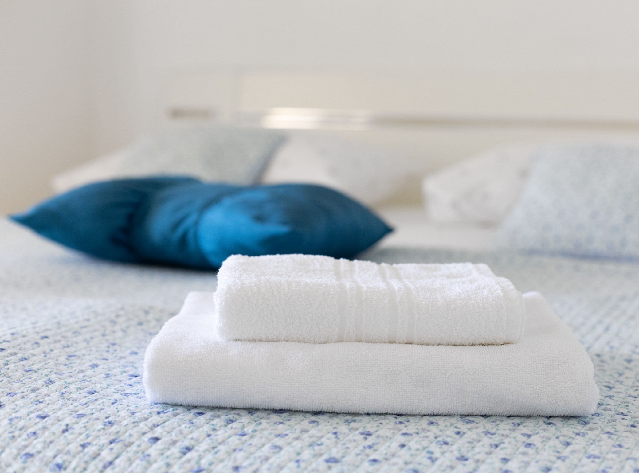 A neatly folded white towel and a blue pillow on a textured blue and white carpet.