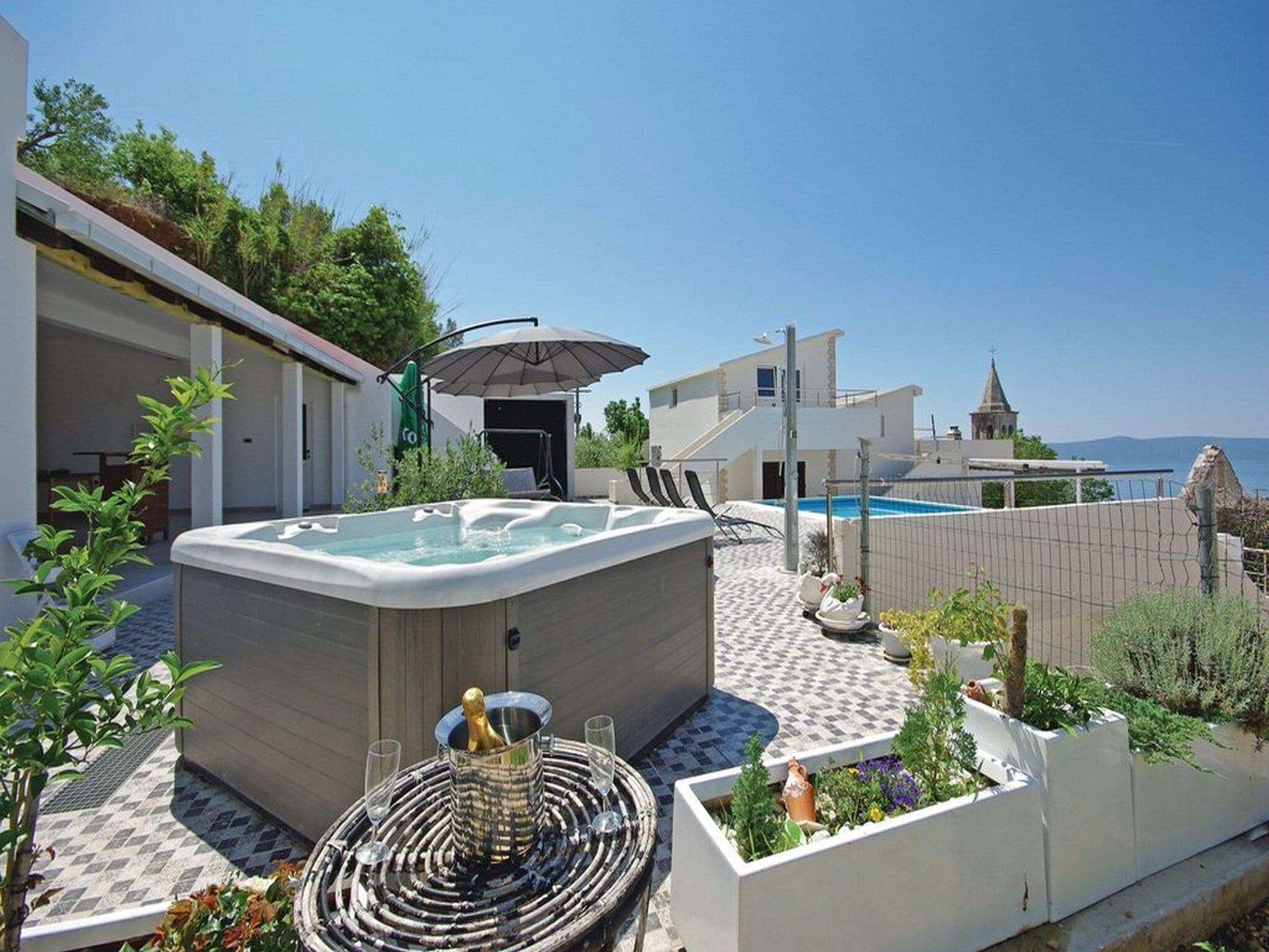 A rooftop pool area with a hot tub, lounge chairs, and a view of the sea.