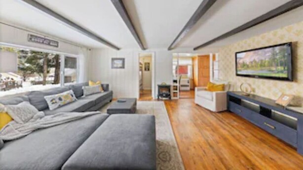 Een moderne woonkamer met een grijze bank, houten vloeren en een televisie aan de muur.