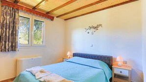 Un dormitorio con techo de madera, una cama con cabecera azul, dos mesitas de noche con lámparas y una ventana con cortinas.