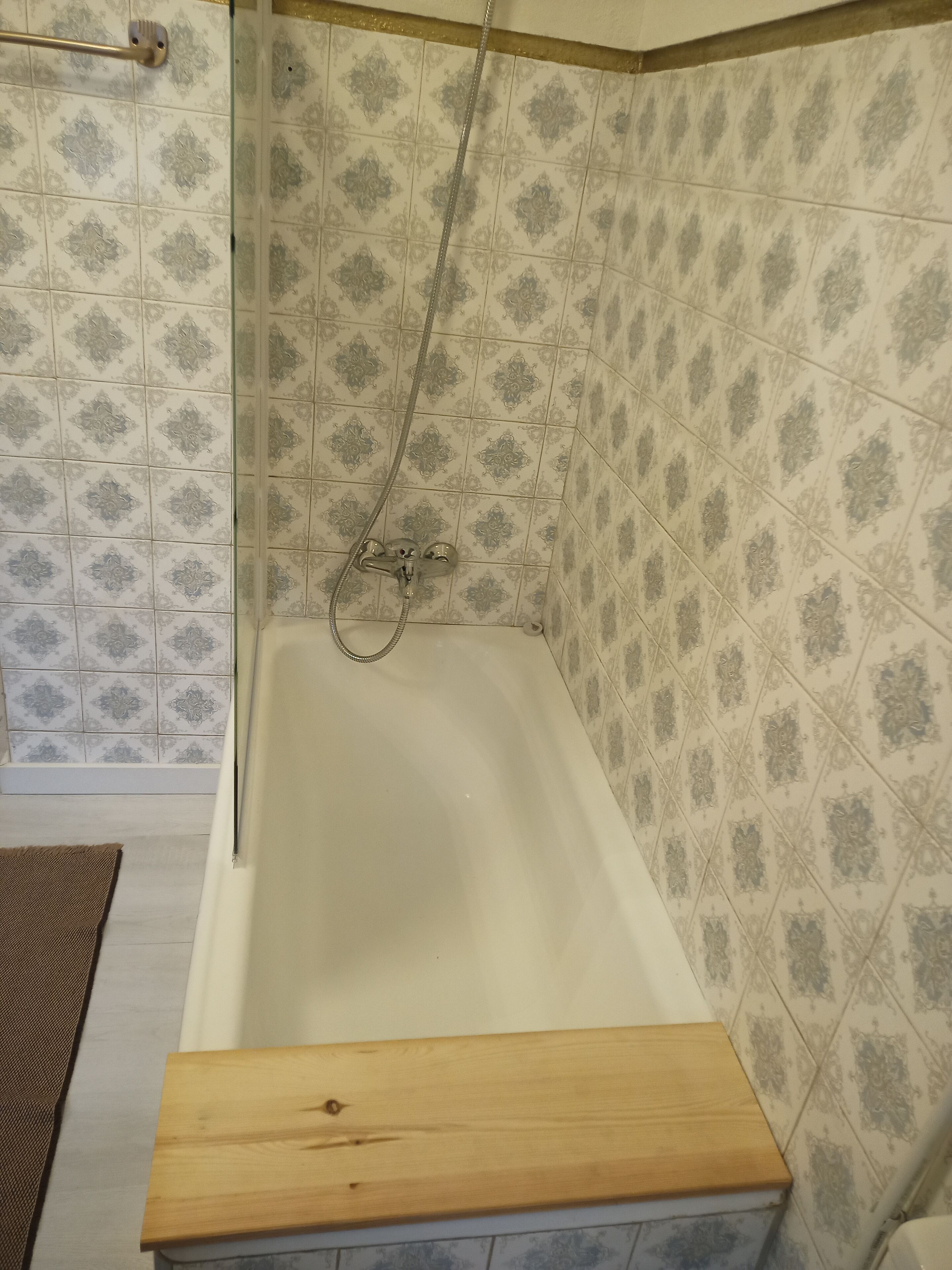 A bathroom with a bathtub, a shower, and patterned tiles.