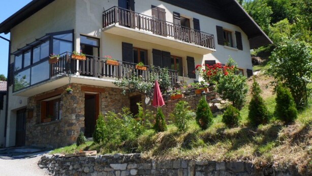 A two-story house with a stone foundation, a balcony with a wooden railing, and a red umbrella. - 42 m2 apartment, ideal for a spa treatment in Brides or skiing in the 3 valleys. (salins fontaine)