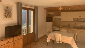 A kitchen with a dining table, chairs, a television on a wooden cabinet, a microwave, and cabinets. - 42 m2 apartment, ideal for a spa treatment in Brides or skiing in the 3 valleys. (salins fontaine)