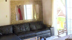 Een kamer met een zwarte leren bank, een houten plafond, een spiegel met een reliëf lijst, een kleine tafel en een stoel.