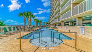 A hotel pool area with lounge chairs, palm trees, and a clear blue sky. - Crescent Shores 1806 - Oceanfront condo rental  (North Myrtle Beach)