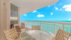A balcony with wicker furniture, a glass table, and a view of the ocean. - Crescent Shores 1806 - Oceanfront condo rental  (North Myrtle Beach)