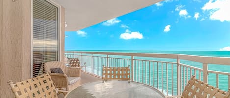 A balcony with wicker furniture, a glass table, and a view of the ocean.