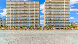A beachfront hotel with multiple balconies, a sandy beach in the foreground, and a clear sky. - Crescent Shores 1806 - Oceanfront condo rental  (North Myrtle Beach)