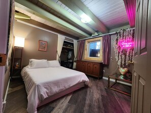 Une chambre à coucher avec un lit, un plancher en bois, une fenêtre avec des rideaux, un panneau lumineux au néon et un cœur décoratif.