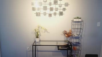 A room with a glass-top table, a metal shelf unit with plants, and a wall-mounted photo display.