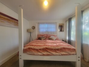 Un lit à baldaquin avec une couvre-lit à motifs, un lampadaire, une fenêtre avec des stores et un tableau encadré accroché au mur.