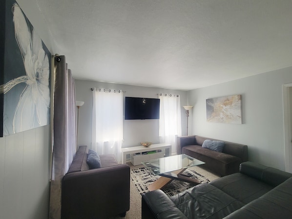 Un salon avec un canapé, une table basse, un téléviseur et un tableau accroché au mur.