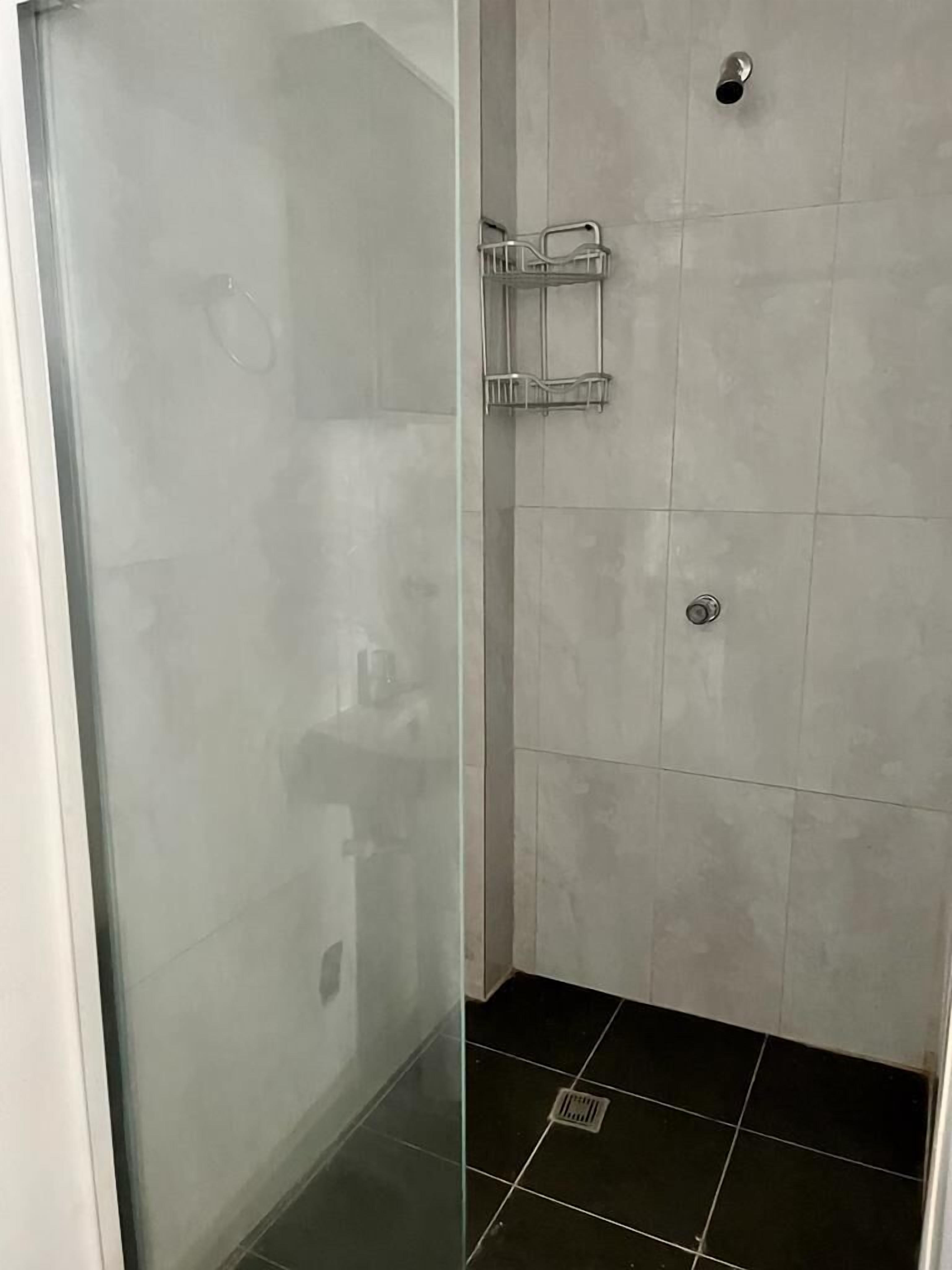 A glass-enclosed shower with a metal rack and a handheld showerhead.
