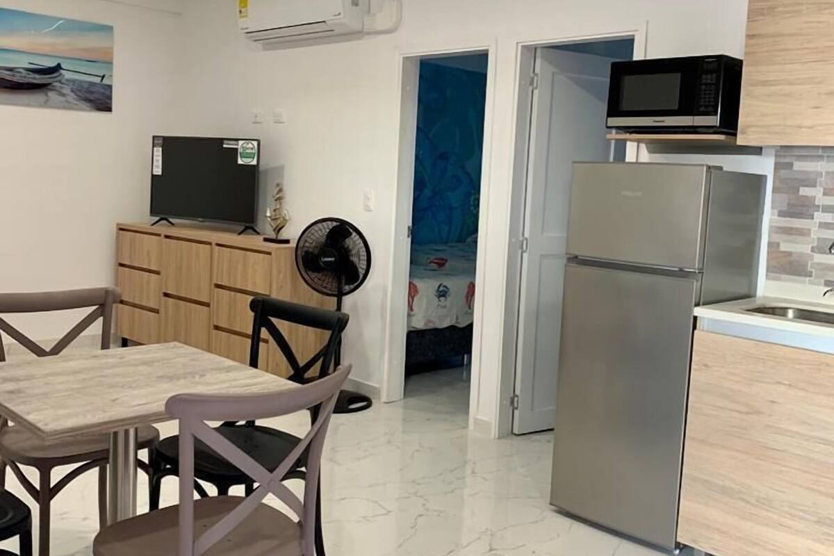 A modern kitchen with a refrigerator, microwave, and dining area with chairs and a table.