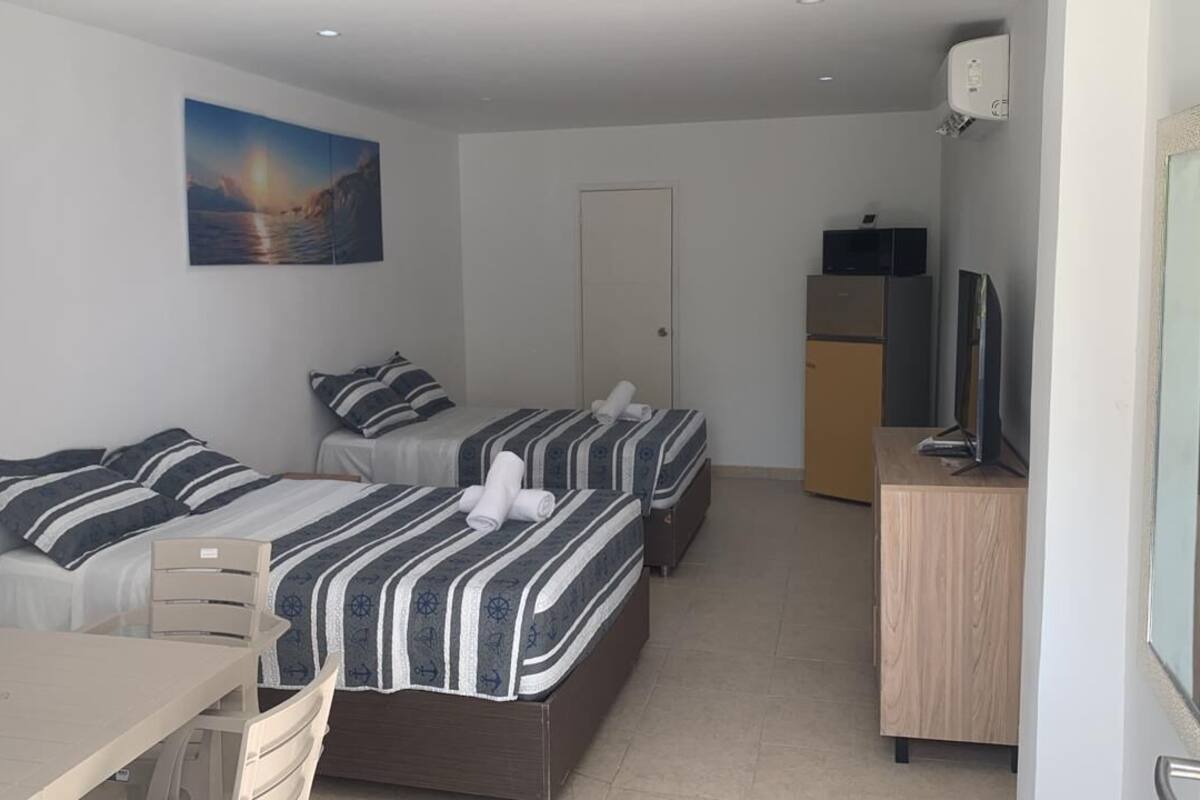 A hotel room with two beds, a desk, a chair, a TV, and a door.