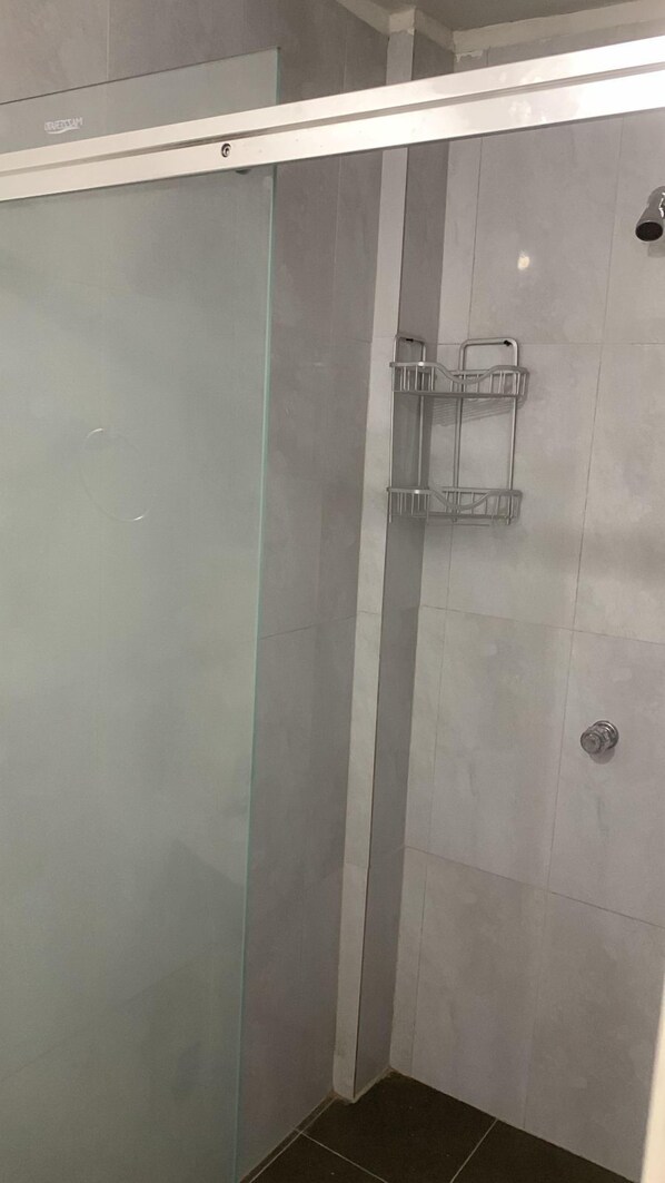 A glass-enclosed shower with a metal rack and a showerhead.