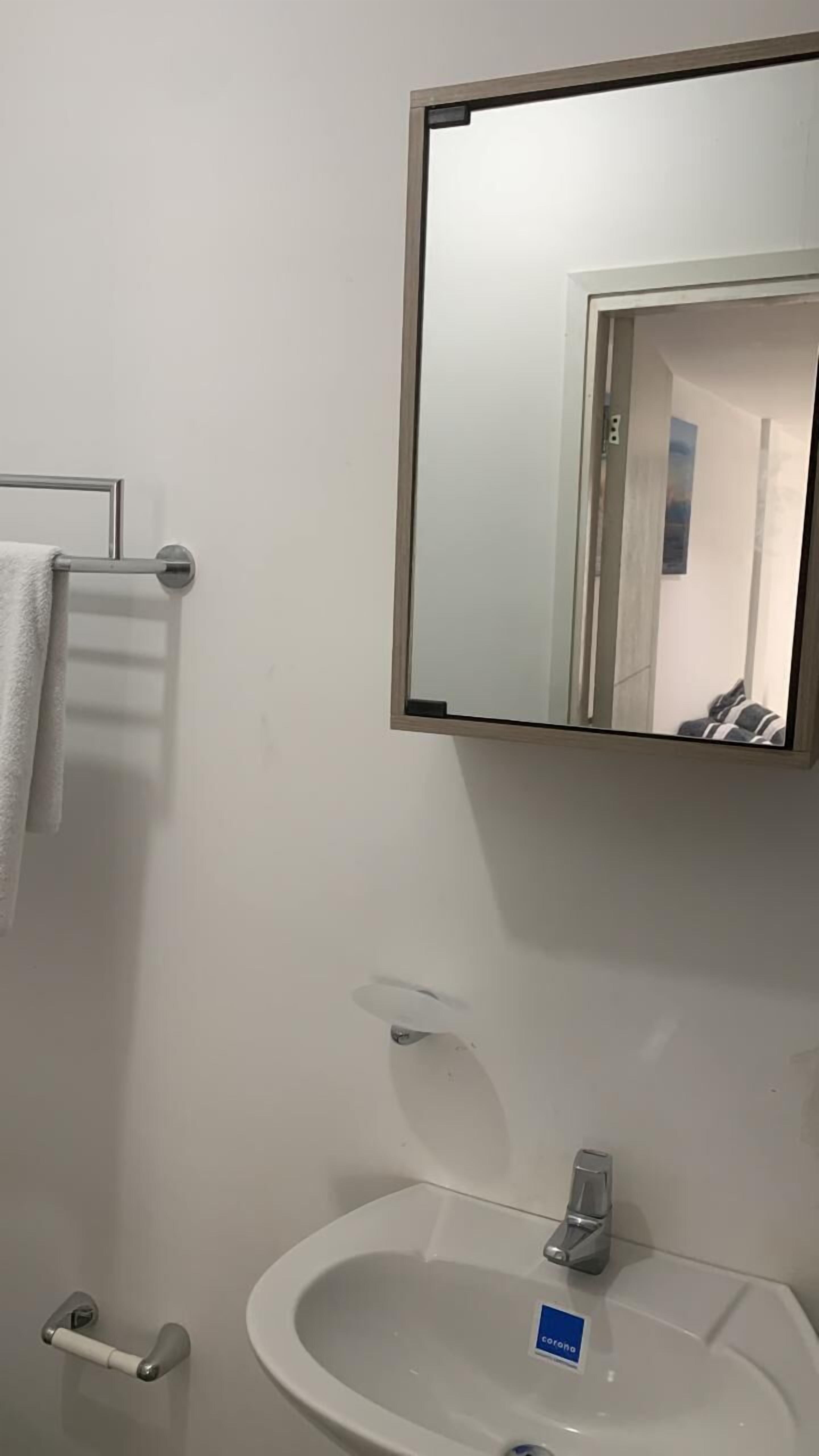Een badkamer met een witte wastafel, een spiegel en een handdoekhouder.