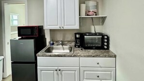 A compact kitchen with white cabinets, a built-in microwave, a coffee maker, and a toaster.