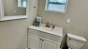 A bathroom with a toilet, sink, mirror, and a window.