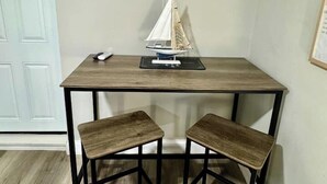 A corner room with a wooden table, two matching stools, and a small sailboat model on the table.