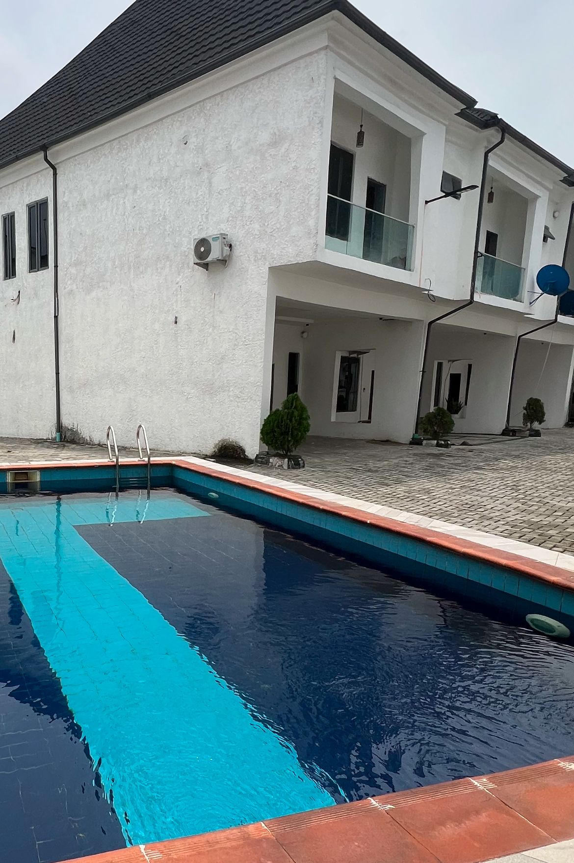 A residential building with a swimming pool, a covered patio, and a satellite dish.
