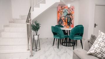 A modern interior with a staircase, a dining area with teal chairs, and a sofa with patterned cushions.