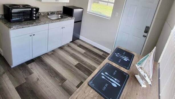 A compact kitchen with white cabinets, a built-in microwave, a sink, and a window with a view of greenery.