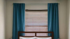 A bed with a leaf-patterned bedspread, a pillow with 'RELAX' text, and blue curtains.