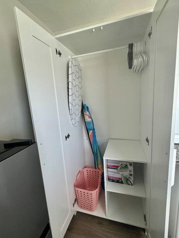 A compact room with a white door, a small shelf with boxes, a pink basket, and a hanging item.