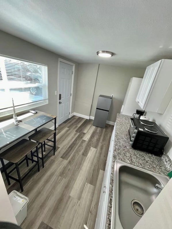 A compact kitchen with a dining table, a refrigerator, a sink, and a window with blinds.