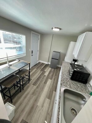A compact kitchen with a dining table, a refrigerator, a sink, and a window with blinds.