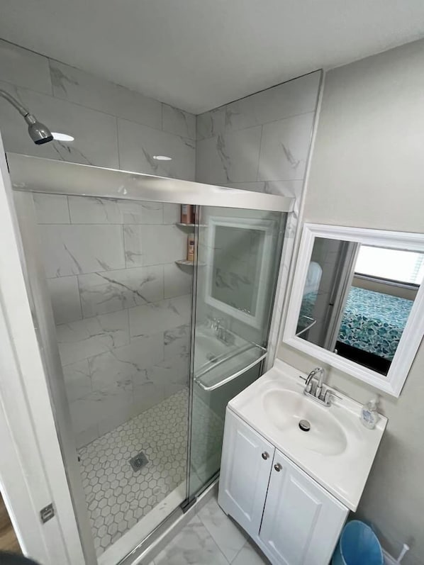 A modern bathroom with a glass-enclosed shower, a white sink with a mirror, and a hexagonal tile floor.
