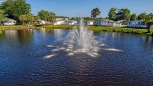 A lake with a fountain in the center, surrounded by houses and greenery. - Pet friendly!  Across from the Pools!  Includes a golf cart! (Surfside Beach)