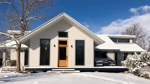 Et moderne hus i to etager med hvide facader, en veranda og en synlig garage.