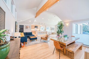 A spacious living area with a large dining table, a sofa, and a kitchen in the background.